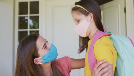 Caucasian-mother-wearing-face-mask-embracing-her-daughter-outside-of-the-house