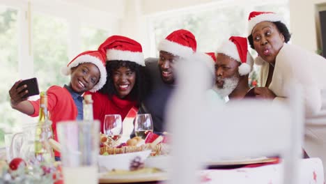 Afroamerikanische-Familie-In-Weihnachtsmützen-Macht-Ein-Selfie-Mit-Dem-Smartphone,-Während-Sie-Am-Esstisch-Sitzt-Ha