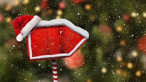 Digital-animation-of-snow-falling-over-santa-hat-on-red-wooden-sign-post-against-christmas-lights