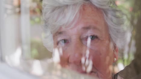 Traurige-ältere-Kaukasische-Frau,-Die-Sich-In-Zeitlupe-Durch-Das-Fenster-Umschaut