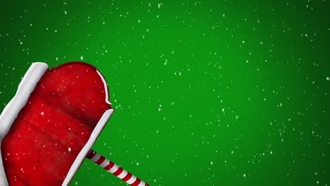 Digital-animation-of-snow-falling-over-santa-hat-on-red-wooden-sign-post-against-green-background