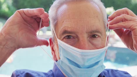 Portrait-of-senior-caucasian-man-with-grey-hair-putting-face-mask-on-looking-at-camera-in-slow-motio