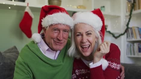 Portrait-of-happy-senior-caucasian-couple-celebrating-christmas-wearing-santa-hats