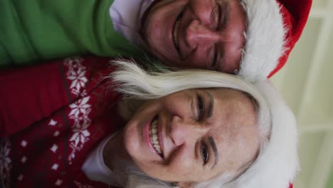 Flipped-sideways-portrait-of-happy-senior-caucasian-couple-celebrating-christmas-wearing-santa-hats
