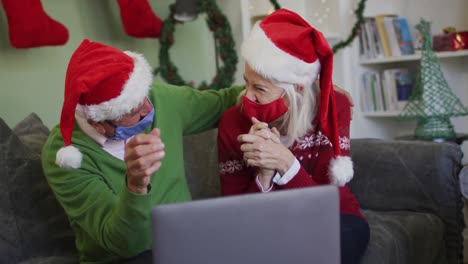 Happy-senior-caucasian-couple-celebrating-christmas-wearing-face-maska-and-santa-hats