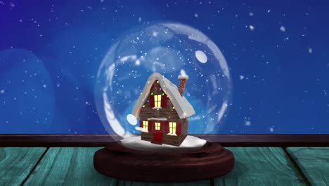 Animation-of-snow-globe-with-house-on-wooden-surface-and-winter-scenery-with-snow-falling
