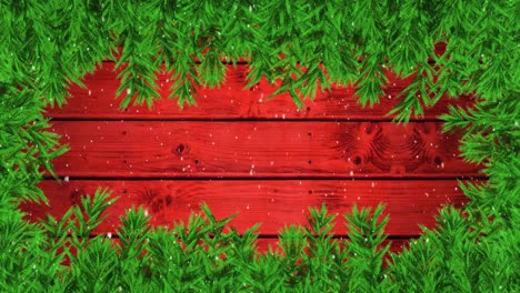 Digital-animation-of-snow-falling-over-green-leaves-forming-a-frame-against-red-wooden-background