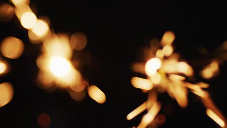 Two-out-of-focus-party-sparklers-sparkling-on-black-background