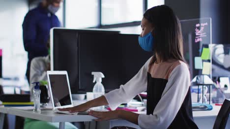 Asiatische-Frau-Mit-Gesichtsmaske-Reinigt-Ihren-Laptop-Mit-Taschentuch-Im-Modernen-Büro