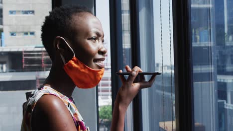 Afroamerikanische-Frau-Mit-Gesichtsmaske-Um-Den-Hals,-Die-Im-Modernen-Büro-Auf-Dem-Smartphone-Spricht