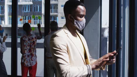 Portrait-of-african-american-man-wearing-face-mask-using-digital-tablet-at-modern-office