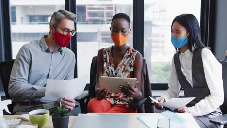Diverse-office-colleagues-wearing-face-masks-discussing-together-at-modern-office