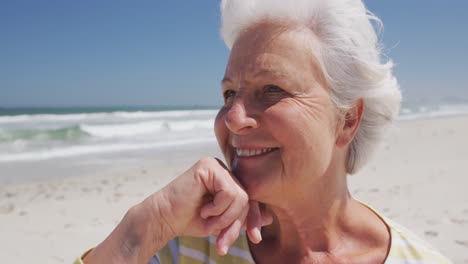 Close-up-of-happy-senior-caucasian-woman-with-hand-on-chin-sitting-on-the-beach-enjoying-the-view