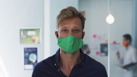 Portrait-of-caucasian-man-adjusting-his-face-mask-at-modern-office