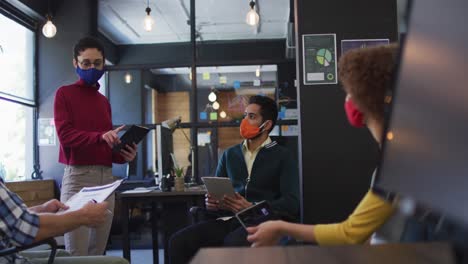Diverse-colleagues-wearing-face-masks-discussing-together-at-modern-office