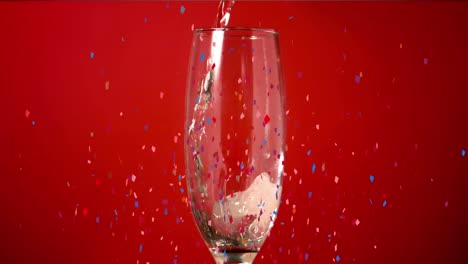 Animation-of-multi-coloured-confetti-falling-over-champagne-flute-on-red