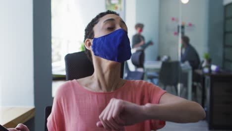 Caucasian-woman-wearing-face-mask-sneezing-on-her-elbow-at-modern-office