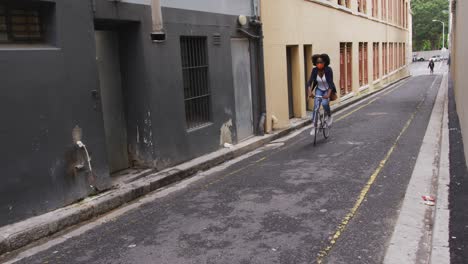 African-american-woman-wearing-face-mask-riding-bicycle-in-street