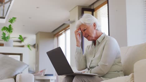 Ältere-Frau,-Die-Einen-Videochat-Auf-Dem-Laptop-Führt,-Während-Sie-Zu-Hause-Auf-Der-Couch-Sitzt