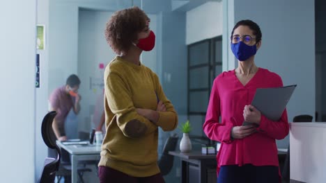 Mixed-race-female-colleagues-wearing-face-masks-in-office