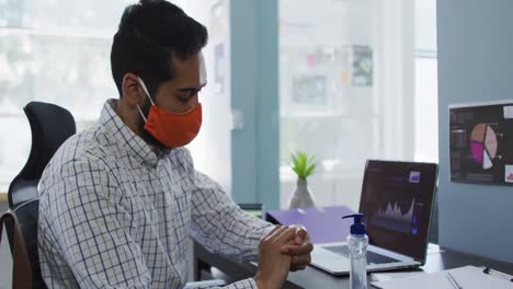 Middle-eastern-man-wearing-face-mask-using-hands-sanitizer-at-modern-office