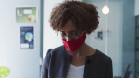 Portrait-of-african-american-woman-wearing-face-mask-holding-temperature-gun-at-modern-office