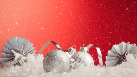 Animation-of-white-christmas-baubles-decorations-with-snow-falling-on-red
