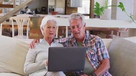 Älteres-Kaukasisches-Paar,-Das-Einen-Videochat-Auf-Dem-Laptop-Führt,-Während-Es-Zu-Hause-Auf-Der-Couch-Sitzt