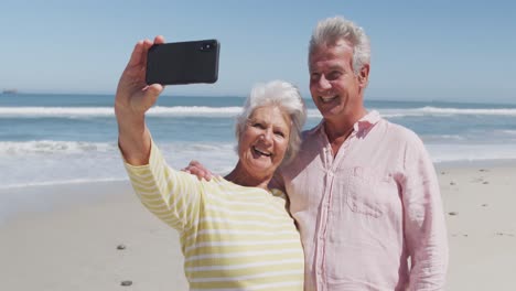 Happy-senior-caucasian-couple-taking-a-selfie-using-smartphone-on-the-beach