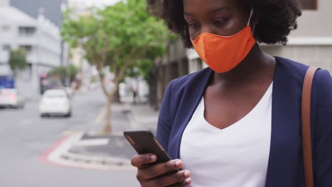 Afroamerikanische-Frau-Mit-Gesichtsmaske-Und-Smartphone-Auf-Der-Straße