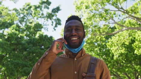 Lächelnder-Afroamerikanischer-Geschäftsmann-Mit-Gesichtsmaske,-Der-Auf-Der-Straße-Auf-Dem-Smartphone-Spricht