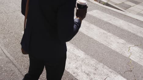Low-section-of-african-american-businessman-carrying-takeaway-coffee-walking-on-zebra-crossing