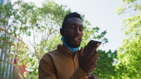 Afroamerikanischer-Geschäftsmann-Mit-Gesichtsmaske,-Der-Auf-Dem-Smartphone-Spricht