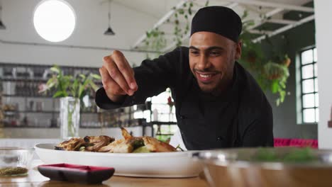 Mixed-race-male-chef-preparing-a-dish-and-smiling-in-a-kitchen-