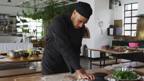 Mixed-race-male-chef-kneading-dough-on-a-kitchen-table