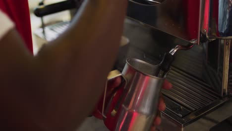 Midsection-of-african-american-barista-using-coffee-machine-frothing-milk-in-cafe