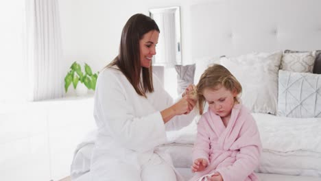 Caucasian-mother-and-daughter-having-fun-brushing-hair-in-bedroom