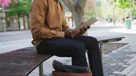 Hombre-De-Negocios-Afroamericano-Con-Mascarilla-Usando-Una-Tableta-Sentada-En-Un-Banco
