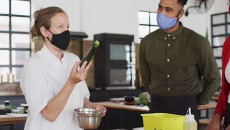 Caucasian-female-chef-teaching-diverse-group-wearing-face-masks