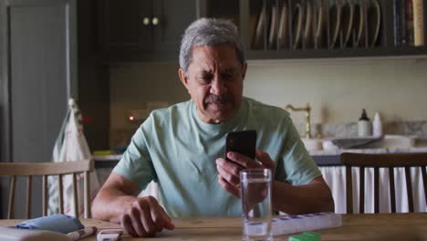 Senior-mixed-race-man-having-video-chat-on-smartphone-in-kitchen
