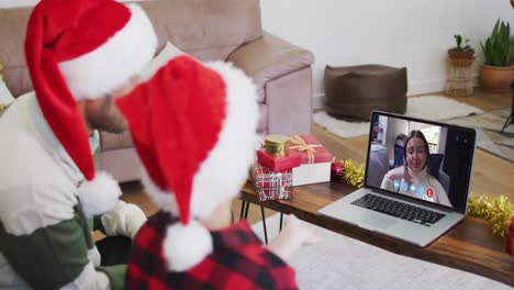 Caucasian-father-and-son-wearing-santa-hats-on-laptop-video-chat-during-christmas-at-home