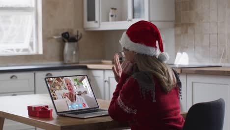 Caucasian-woman-wearing-santa-hat-on-laptop-video-call-during-christmas-at-home