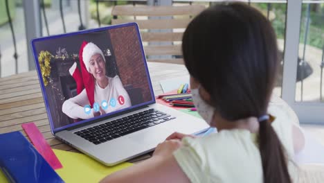 Caucasian-girl-wearing-face-mask,-using-laptop-on-video-chat-with-woman-during-christmas-at-home