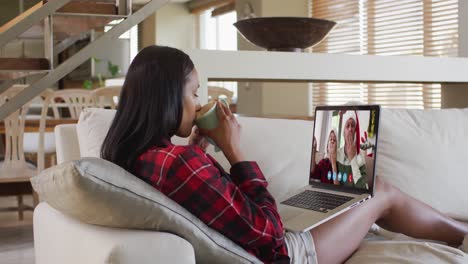 Mixed-race-woman-using-laptop-on-video-chat-with-friends-during-christmas-at-home