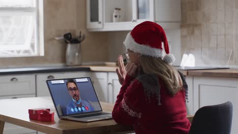 Caucasian-woman-wearing-santa-hat-on-laptop-video-call-during-christmas-at-home
