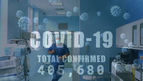 Animation-of-covid-19-text-and-numbers-and-cells-over-medical-staff-in-hospital