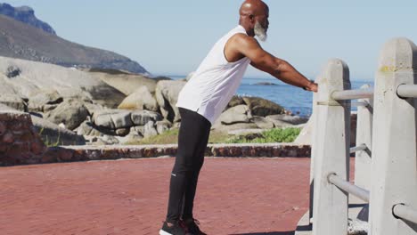 Senior-african-american-man-exercising-stretching-on-rocks-by-the-sea