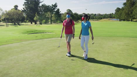 Two-caucasian-women-playing-golf-wearing-face-masks-walking-together