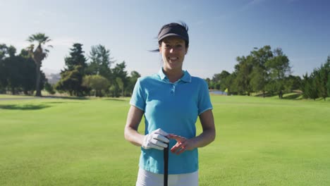 Portrait-of-female-caucasian-golf-player-smiling-while-standing-with-golf-club-at-golf-course