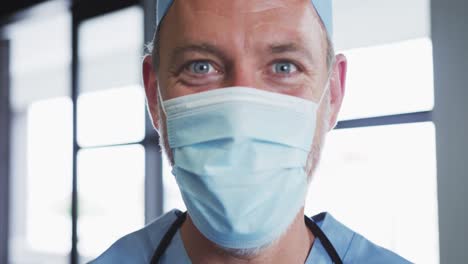 Portrait-of-caucasian-male-doctor-wearing-face-mask-looking-at-camera-